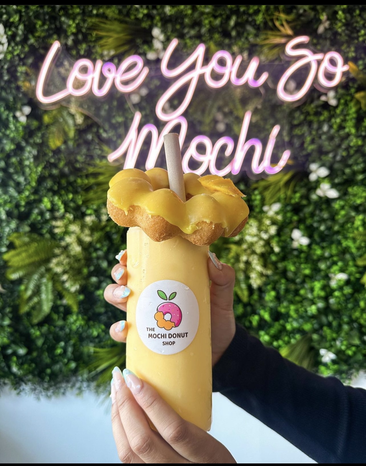 Mango smoothie topped with a mochi donut in front of the 'Love You So Mochi' neon sign